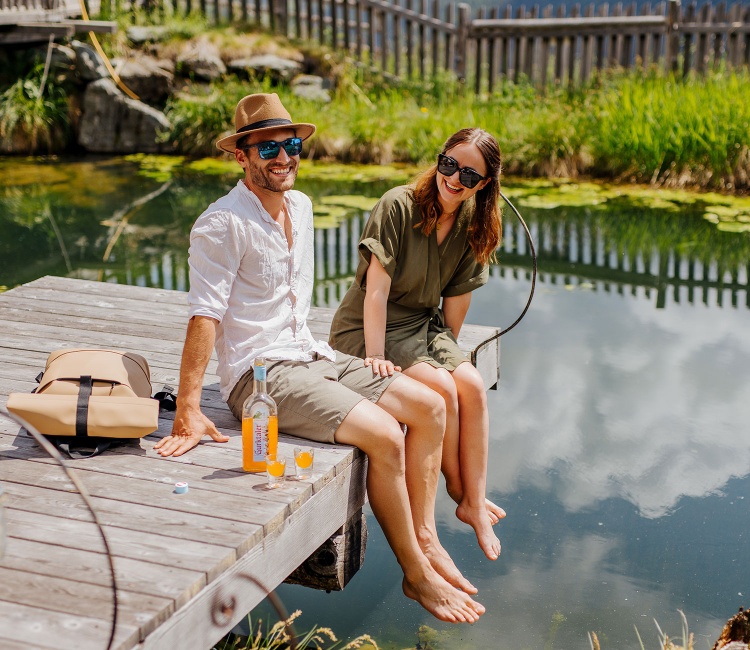 Junges Paar sitzt an einem Steg und trinken Gurktaler Alpen-Aperitif